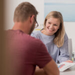 Dr. Janina Ledderose sitzt mit einem männlichen Patienten am Tisch und berät diesen lächelnd